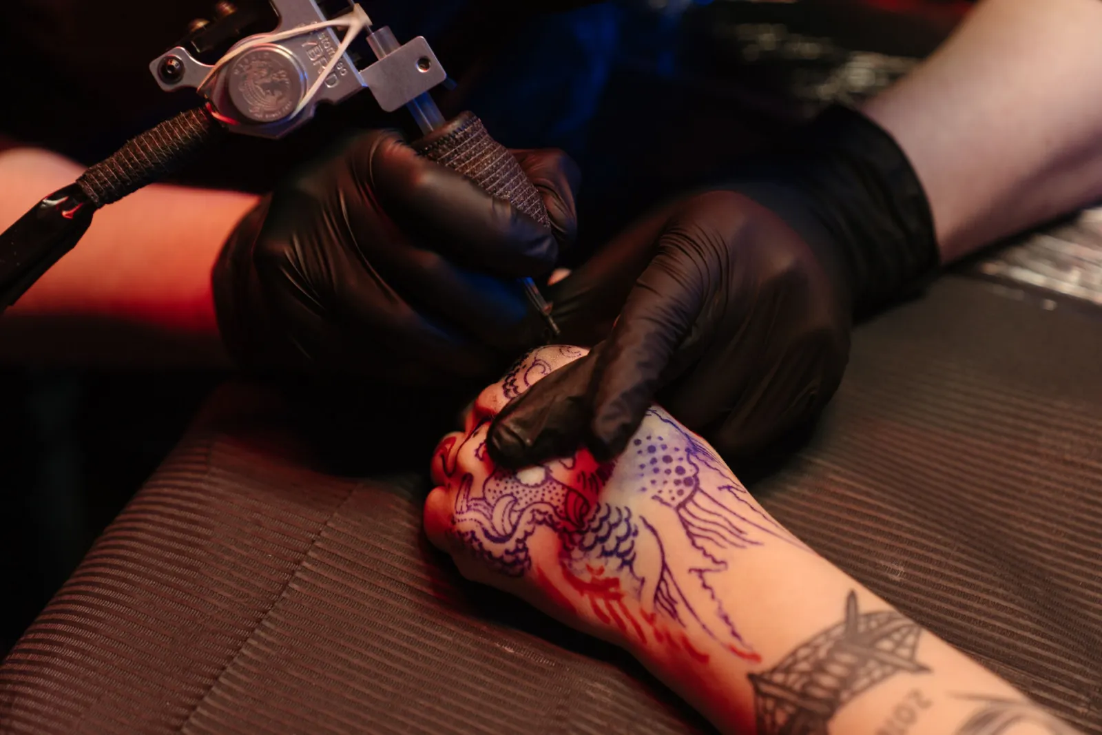Tätowierer sticht ein Tattoo auf einer Hand im Studio